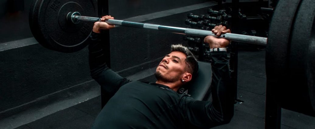 Man performing bench press with heavy barbell in a gym setting, focusing on strength training.